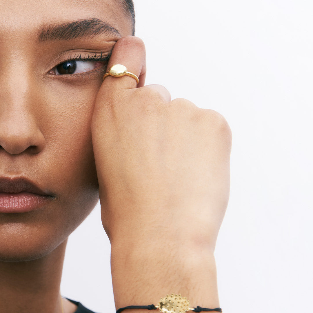 Pulseira ajustável de algodão com detalhe com relevos em prata 925 com banho de ouro 18k em modelo.