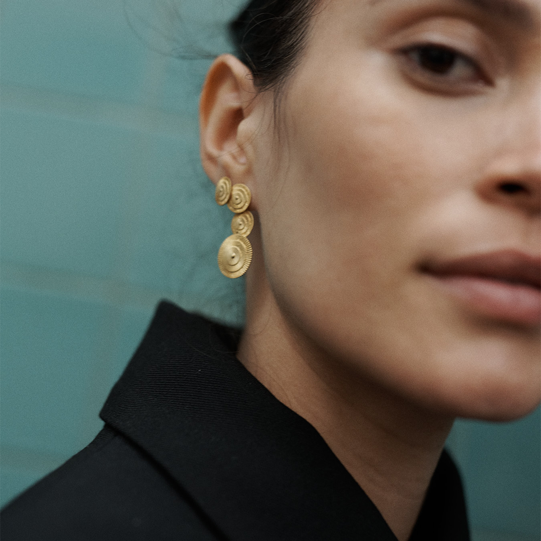 Brincos compridos articulados com detalhes redondos e relevo em prata 925 com banho de ouro 18K em modelo.