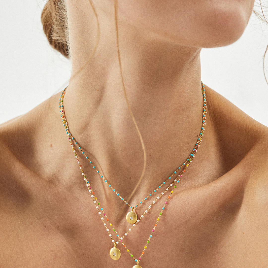 Colar de esferas em esmalte e pendente em prata 925 com banho de ouro 18K e zircónia cúbica em modelo.